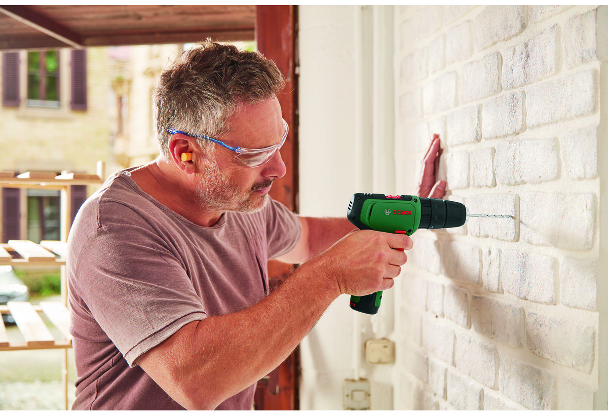 Απεικονίζεται άνδρας να χρησιμοποιεί το δραπανοκατσάβιδο στον τοίχο.